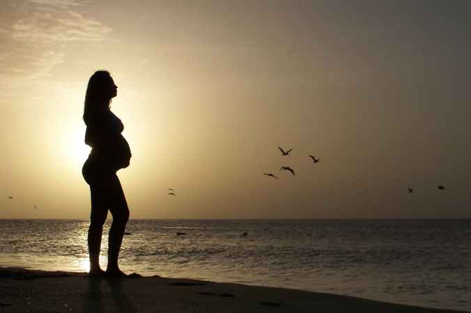 silhouette of pregnant standing on seashore during golden hour