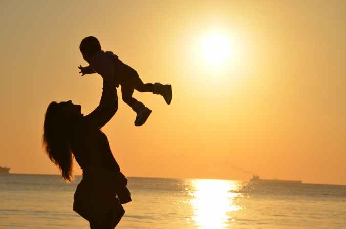 woman carrying baby at beach during sunset
