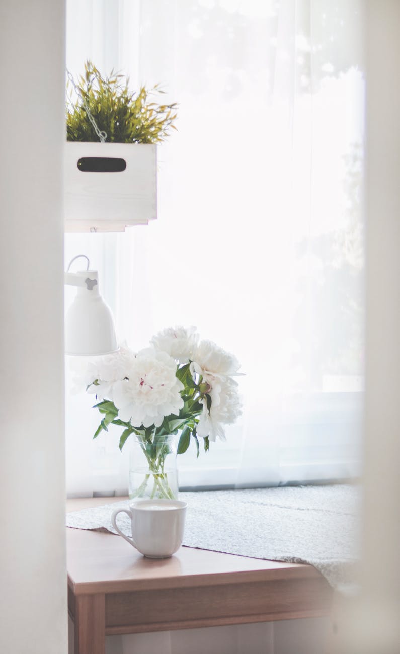 white peonies in clear glass vase centerpiece near a white ceramic mug closeup photography